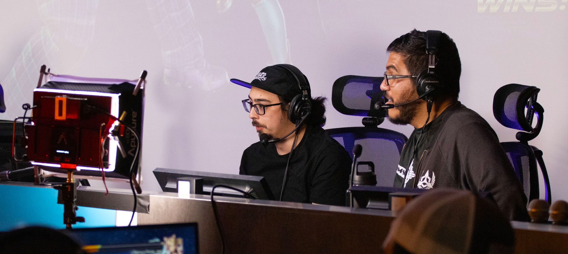 Two young men in headsets play games competitively sitting at computers.